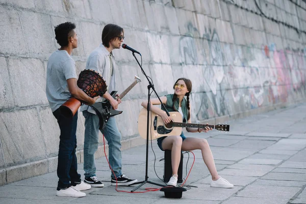 Team of young friends playing guitars and djembe in urban environment — Stock Photo