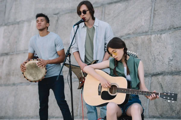 Young and happy male and female street musicians playing guitars and djembe in city — Stock Photo