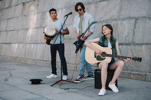 Chica joven y hombres multirraciales con instrumentos musicales que actúan en la calle soleada de la ciudad - foto de stock