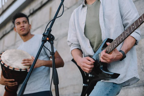 Joven feliz macho buskers jugando guitarra y djembe en la calle de la ciudad - foto de stock