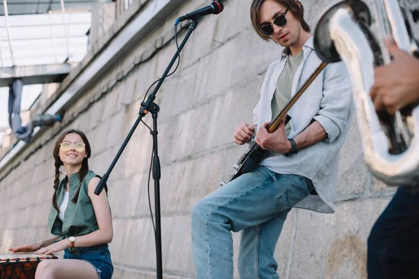 Jóvenes buskers felices con guitarra, tambor y saxofón en la calle de la ciudad - foto de stock