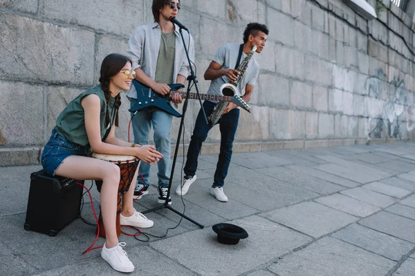 Молодая счастливая женщина с барабаном и мужчины с гитарой и джембой на городской улице — стоковое фото