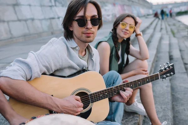 Молодая счастливая девушка слушает мужчину, играющего на гитаре на городской улице — стоковое фото