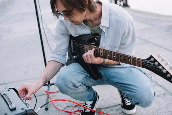 Jovem homem ajustando amplificador de guitarra enquanto se apresenta na rua — Fotografia de Stock