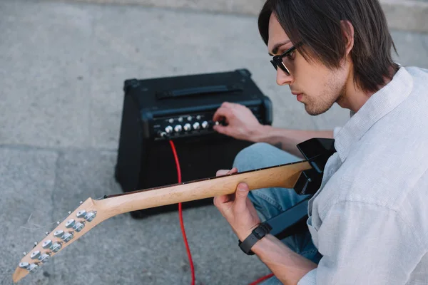 Busker ajustant amplificateur de guitare tout en effectuant sur la rue ensoleillée de la ville — Photo de stock