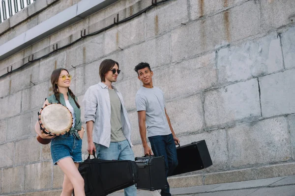 Мультирасовий музичний гурт, що ходить та несе музичні інструменти на сонячній вулиці міста — стокове фото