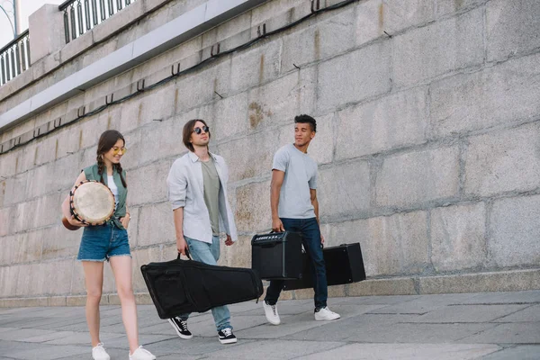 Jóvenes buskers felices caminando y llevando instrumentos musicales en la calle de la ciudad - foto de stock