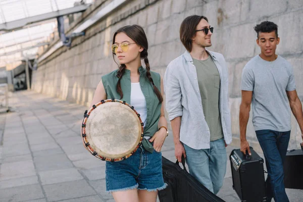 Team di giovani amici maschi e femmine che camminano e trasportano strumenti musicali in ambiente urbano — Foto stock