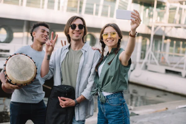 Jóvenes y felices músicos callejeros con instrumentos tomando selfies en la ciudad - foto de stock