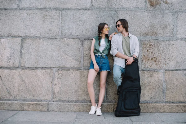 Joven pareja feliz con la guitarra mirándose en la calle de la ciudad - foto de stock