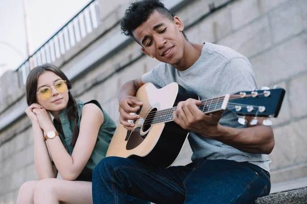 Hübsches Mädchen hört afrikanisch-amerikanischem Mann beim Gitarrespielen in städtischer Umgebung zu — Stockfoto