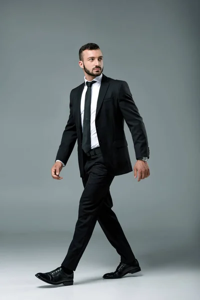 Handsome businessman in suit walking and looking away on grey — Stock Photo