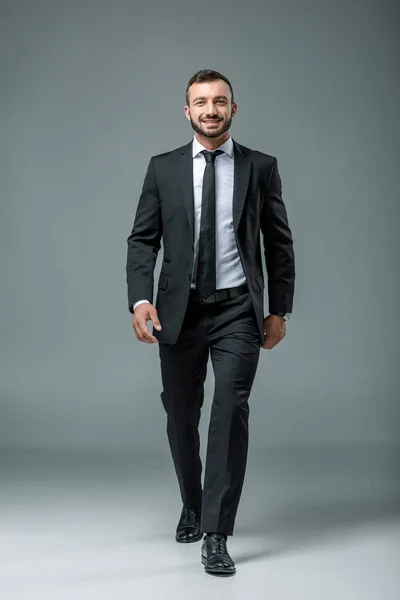 Smiling handsome businessman walking on grey — Stock Photo