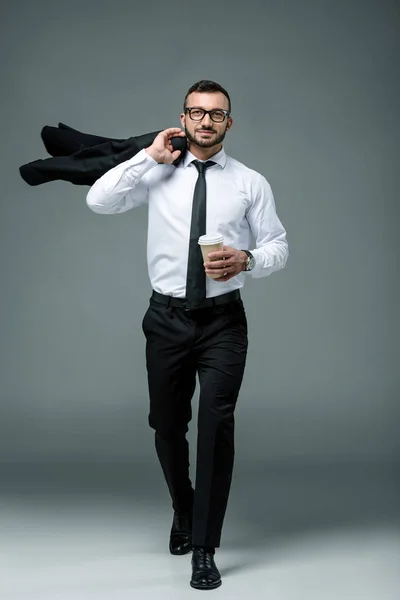 Hombre de negocios guapo caminando con taza de café desechable en gris — Stock Photo