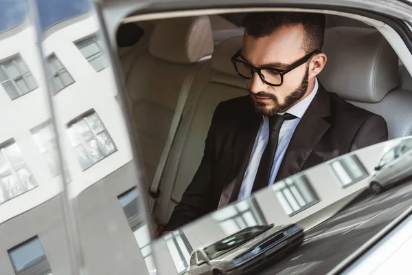 Hombre de negocios guapo sentado en el coche y mirando hacia abajo - foto de stock