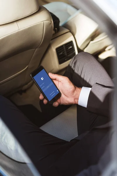 Cropped image of businessman holding smartphone with loaded facebook page in car — Stock Photo