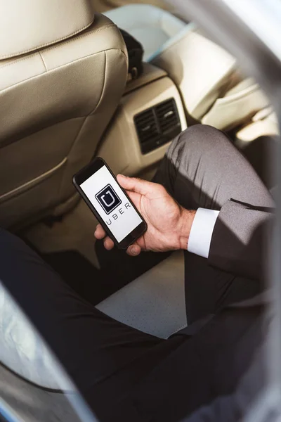 Cropped image of businessman holding smartphone with loaded uber page in car — Stock Photo