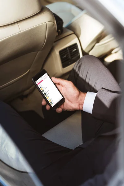 Image recadrée de l'homme d'affaires tenant smartphone avec appareil de musique pomme dans la voiture — Photo de stock