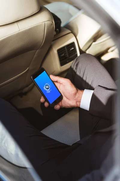 Imagen recortada de hombre de negocios sosteniendo teléfono inteligente con página Shazam cargado en el coche - foto de stock