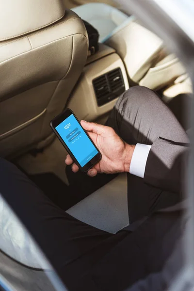 Cropped image of businessman holding smartphone with loaded skype page in car — Stock Photo