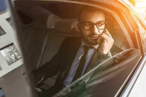 Handsome businessman sitting in car and talking by smartphone — Stock Photo