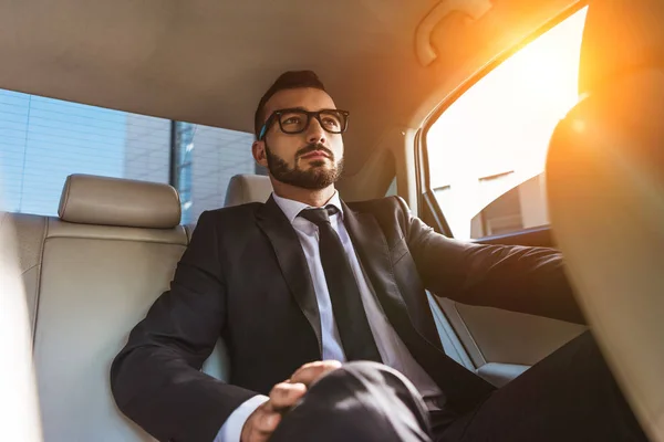 Homem de negócios bonito em terno sentado no carro durante o pôr do sol — Fotografia de Stock