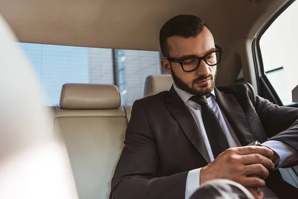 Красивый бизнесмен проверяет время на наручные часы в машине — стоковое фото