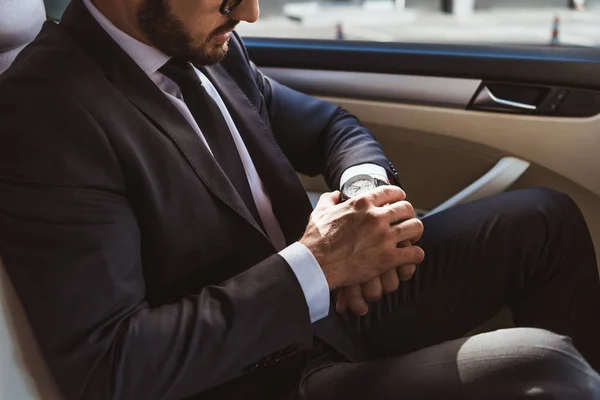 Imagem cortada de homem de negócios em terno verificando o tempo no relógio de pulso no carro — Fotografia de Stock
