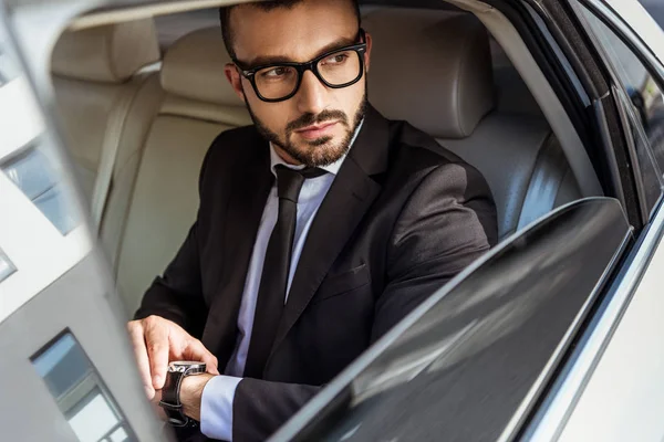 Bel homme d'affaires vérifiant le temps sur montre-bracelet dans la voiture et détournant les yeux — Photo de stock