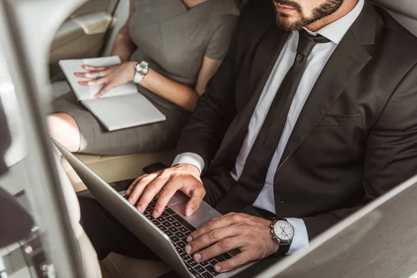 Обрезанный образ бизнесмена, работающего с ноутбуком в машине, секретаря, сидящего с ноутбуком — стоковое фото