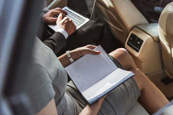 Cropped image businessman and assistant working in car with laptop and notebook — Stock Photo