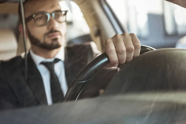 Selective focus of handsome driver in suit driving car — Stock Photo