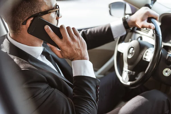 Side view of handsome driver in suit driving car and talking by smartphone — Stock Photo