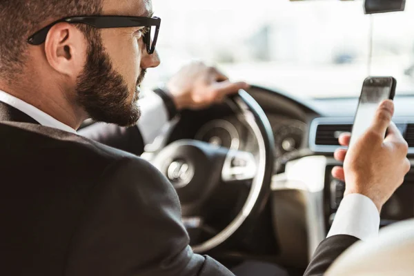 Beau conducteur en costume voiture de conduite et tenant smartphone — Photo de stock