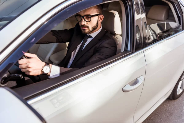 Красивый водитель в костюме и очках за рулем автомобиля — стоковое фото