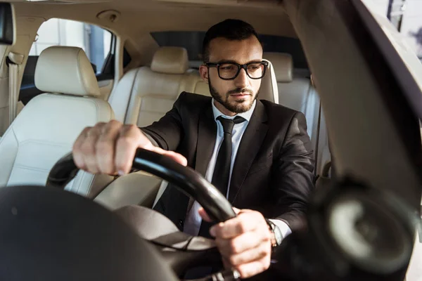 Handsome driver in suit driving car and looking at side mirror — Stock Photo