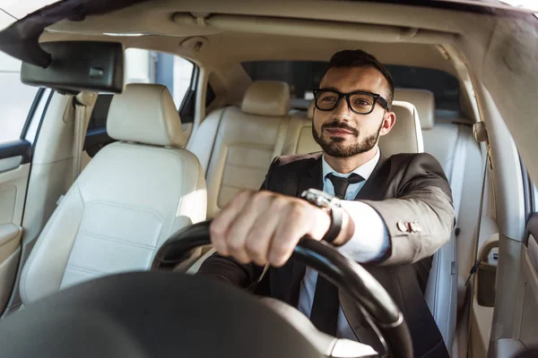 Joyeux beau chauffeur en costume et lunettes voiture de conduite — Photo de stock