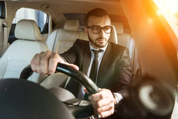 Schöner Fahrer in Anzug und Brille beim Autofahren während des Sonnenuntergangs — Stockfoto