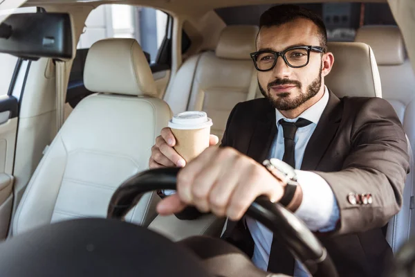 Schöner Fahrer im Anzug, der Auto fährt und Kaffee in Pappbecher hält — Stockfoto