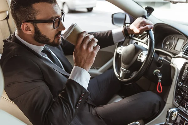 Conductor guapo en traje coche de conducción y beber café en taza de papel - foto de stock