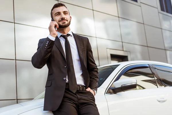 Bello uomo d'affari parlando da smartphone e in piedi vicino auto sulla strada — Foto stock