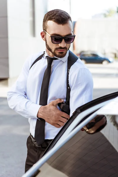 Gutaussehender Wachmann berührt Waffe und öffnet Autotür — Stockfoto