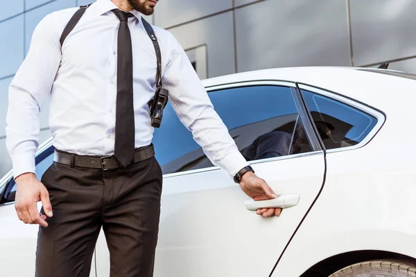 Cropped image of security guard with gun opening car door — Stock Photo