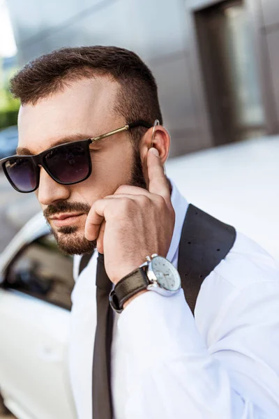 Handsome security guard listening message with security earpiece on street near auto — Stock Photo