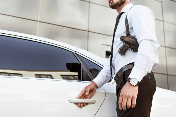 Cropped image of security guard with gun opening auto door — Stock Photo