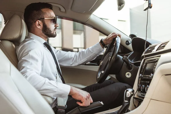 Visão lateral do motorista bonito em óculos de sol condução automática — Fotografia de Stock