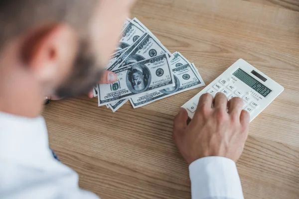 Geschnittenes Bild eines Unternehmensberaters, der Dollar mit Taschenrechner im Büro zählt — Stockfoto