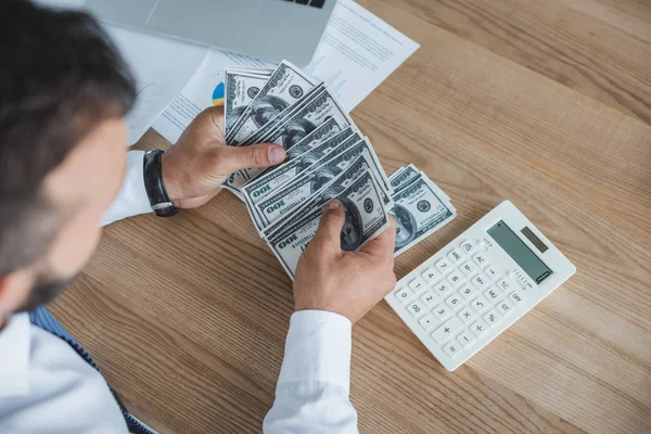 Обрезанное изображение финансиста, подсчитывающего наличные с помощью калькулятора в офисе — стоковое фото