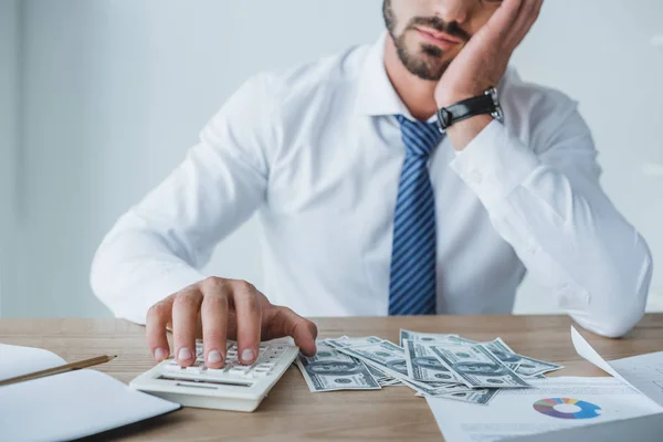 Image recadrée de financier fatigué comptant de l'argent avec calculatrice dans le bureau — Photo de stock