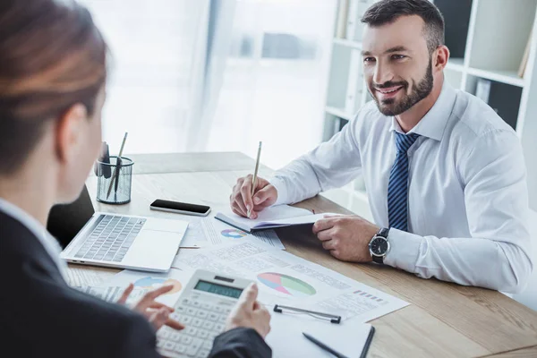 Financieros sonrientes mirándose durante el trabajo en la oficina - foto de stock